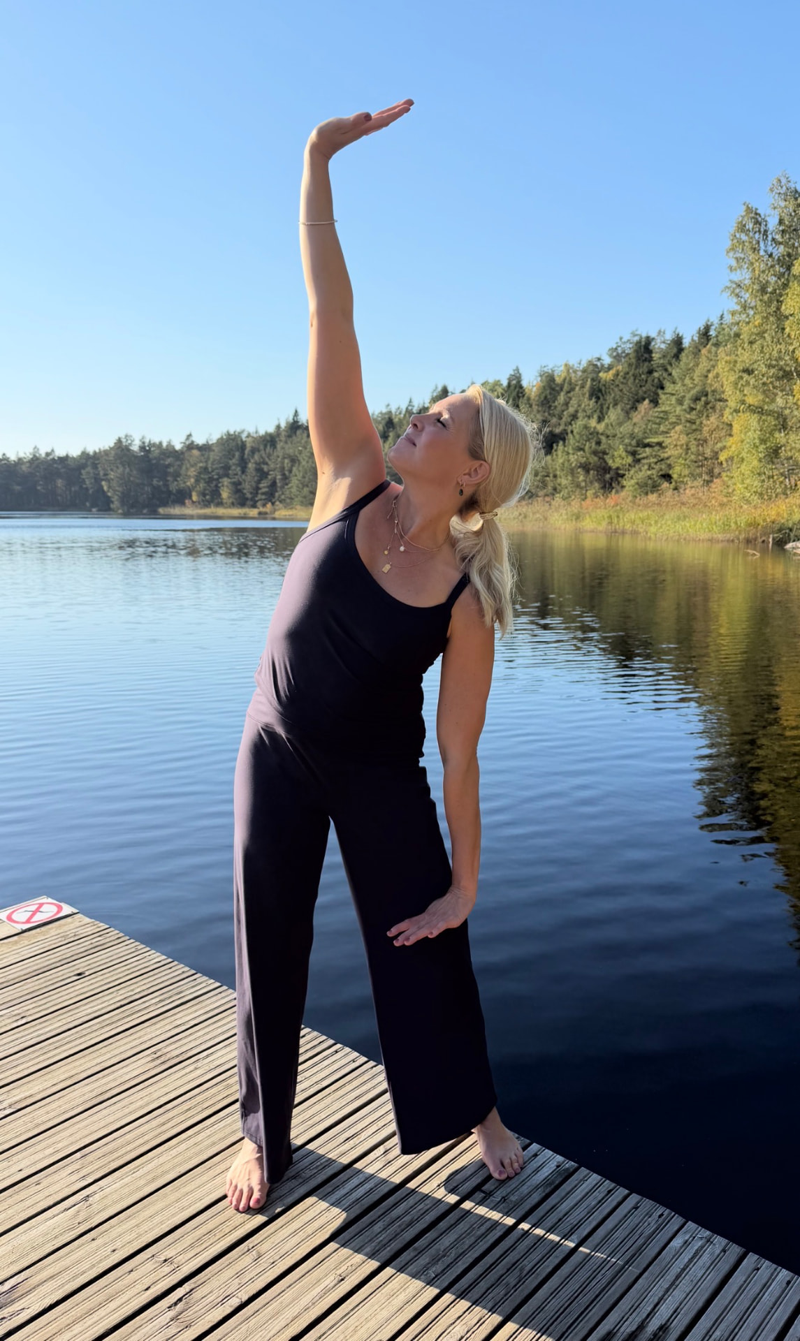 Johanna sträcker en arm mot himlen i qigong vid sjön